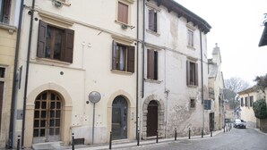 A historic building with arched doorways and windows, a cobblestone street, and a parked car.