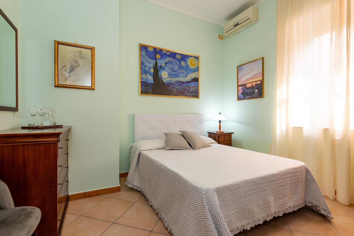 Un dormitorio con cama, cómoda, mesita de noche y dos cuadros en la pared.