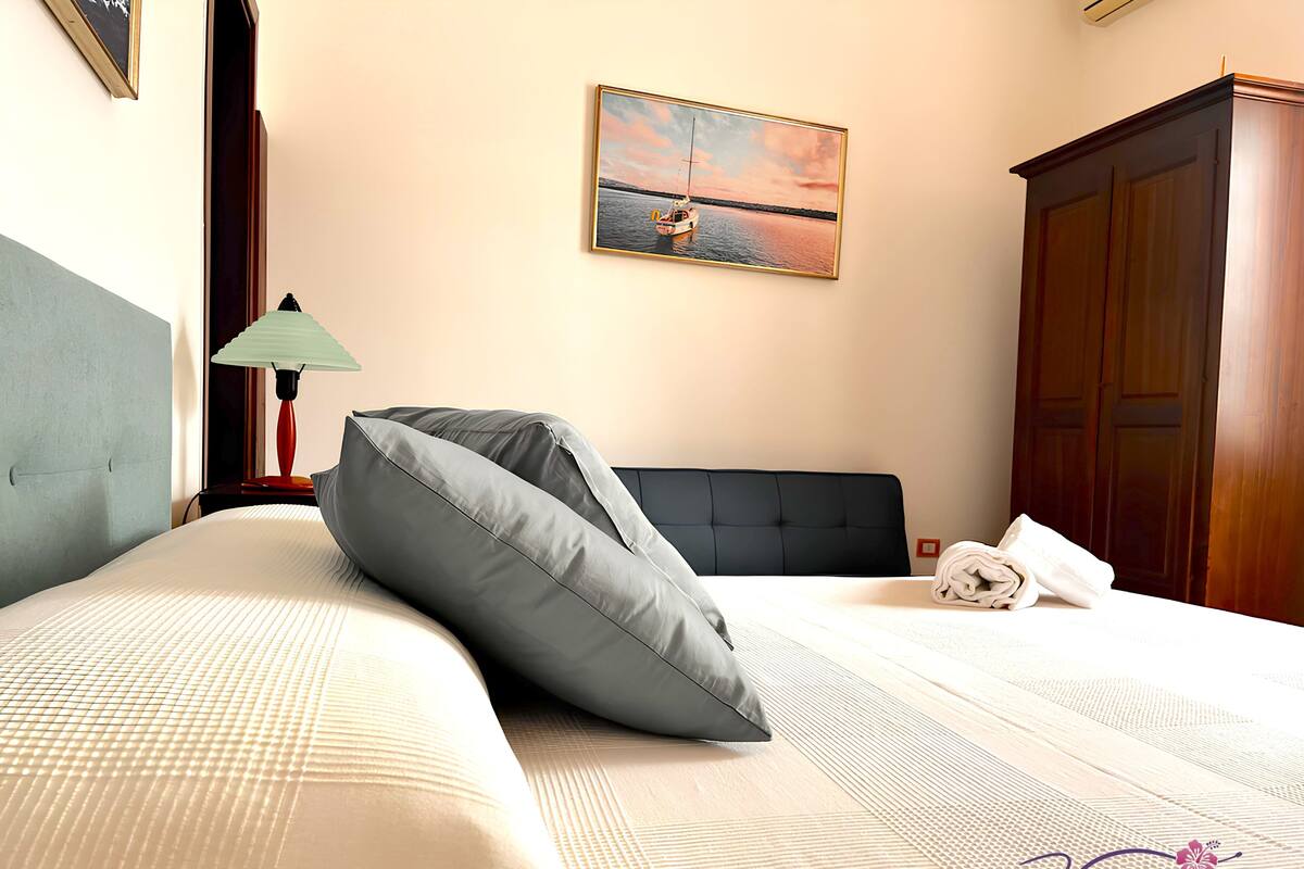 Una habitación de hotel con cama, un cuadro de un barco en el agua, un armario de madera y una lámpara.