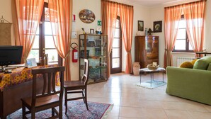 A living room with a green sofa, wooden dining table, and chairs, a television, and a bookshelf. - B&B Hibiscus (Agropoli)