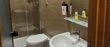 A bathroom with a shower, two toilets, a sink, and a mirror.