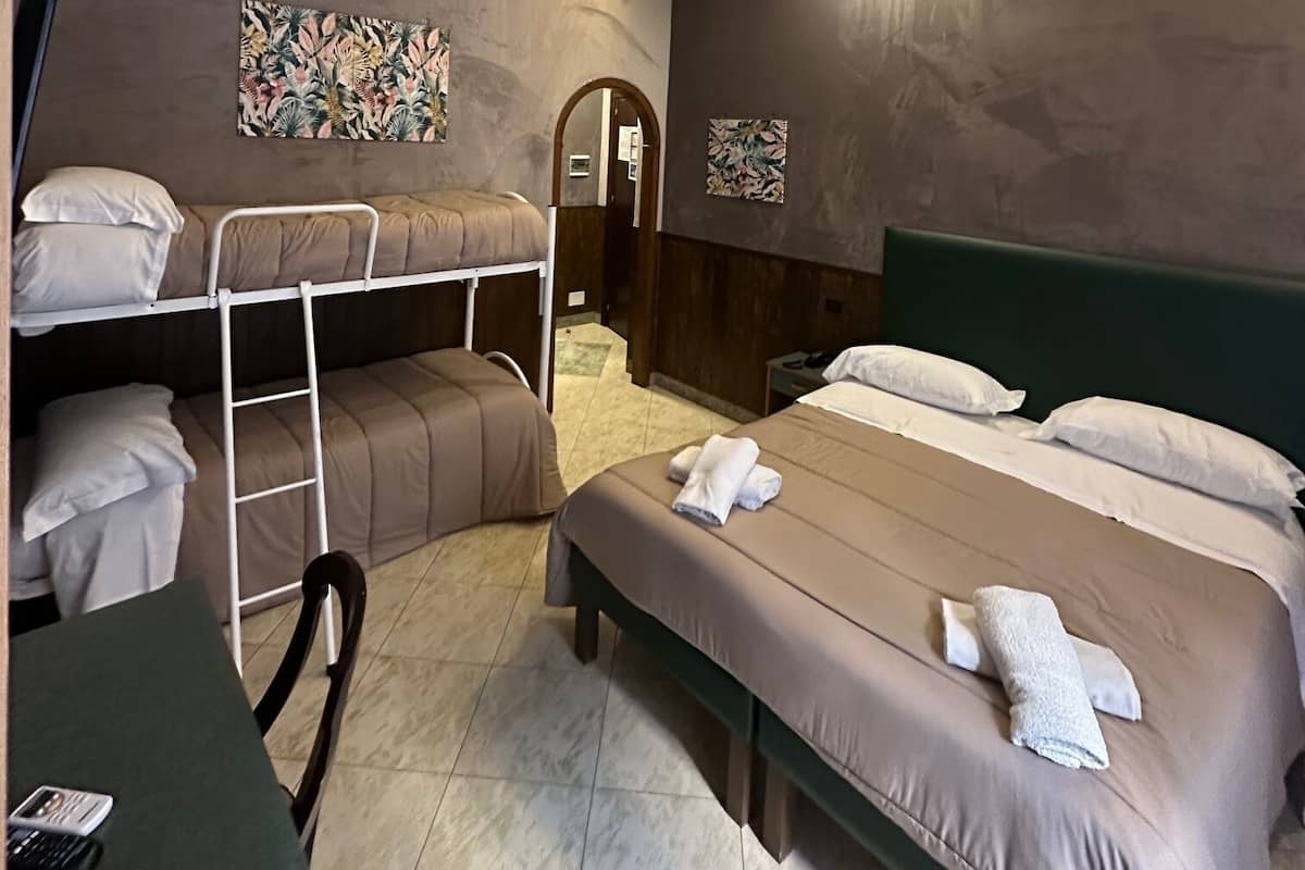A hotel room with bunk beds, a desk with a chair, and a bed with towels.
