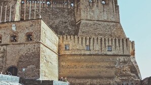 A historic stone fortress with a large central tower and a fortified wall, situated by a body of water. - Smart station hotel  (Naples)