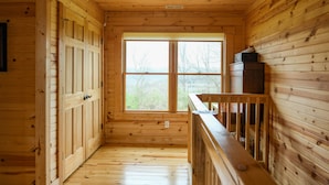 L’intérieur d’un chalet en bois, avec une grande fenêtre, des murs en bois et une rambarde en bois.