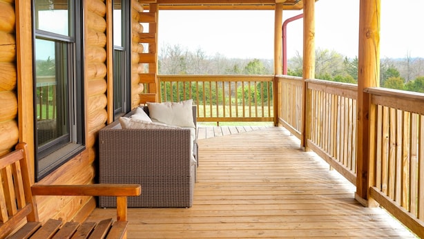 Une terrasse en bois avec un banc et un canapé, une rambarde et une vue sur l’extérieur.