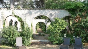 A garden with a stone archway, two lounge chairs, and a pathway leading through it.