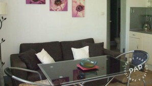 A living room with a dark brown sofa, a glass coffee table with a bowl, and three wall-mounted flower paintings.