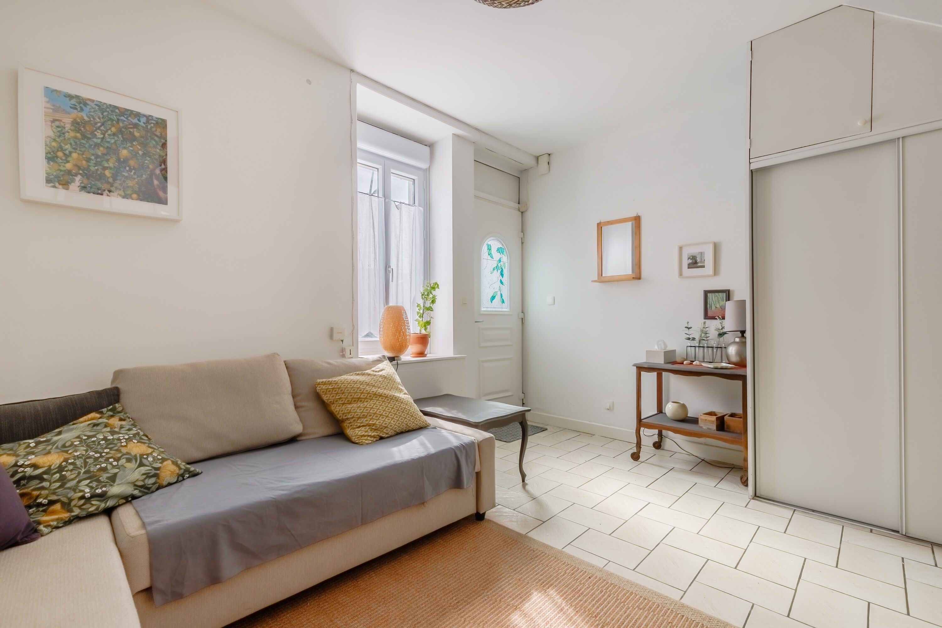 A compact living space with a sofa, a small table, a potted plant, and a shelf with decorative items.