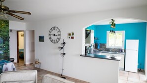 Uma cozinha moderna com uma parede azul decorativa, um relógio grande e uma área de refeições com ventilador de teto.