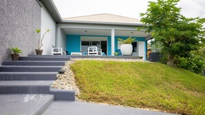 Uma casa moderna com fachada azul, escadaria de pedra e um gramado frontal.