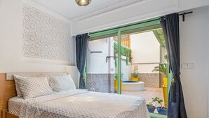 Un dormitorio con cama, lámpara colgante y vistas a un espacio exterior con piscina y plantas en macetas.