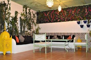 Experience the vibrant colors and traditional Moroccan style in this beautifully designed room, featuring a low sofa, green metal-framed table and chair, and a stunning floral arrangement.