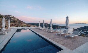 A rooftop infinity pool with lounge chairs and umbrellas, overlooking a mountainous landscape. - Melianthos Villas (Sifnos)