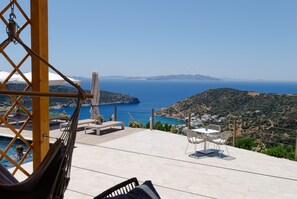 A terrace with a pool, outdoor seating, and a view of the sea and hills. - Melianthos Villas (Sifnos)