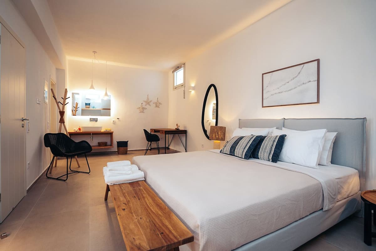 Quarto moderno com uma cama grande, um banco de madeira, uma escrivaninha e uma cadeira.