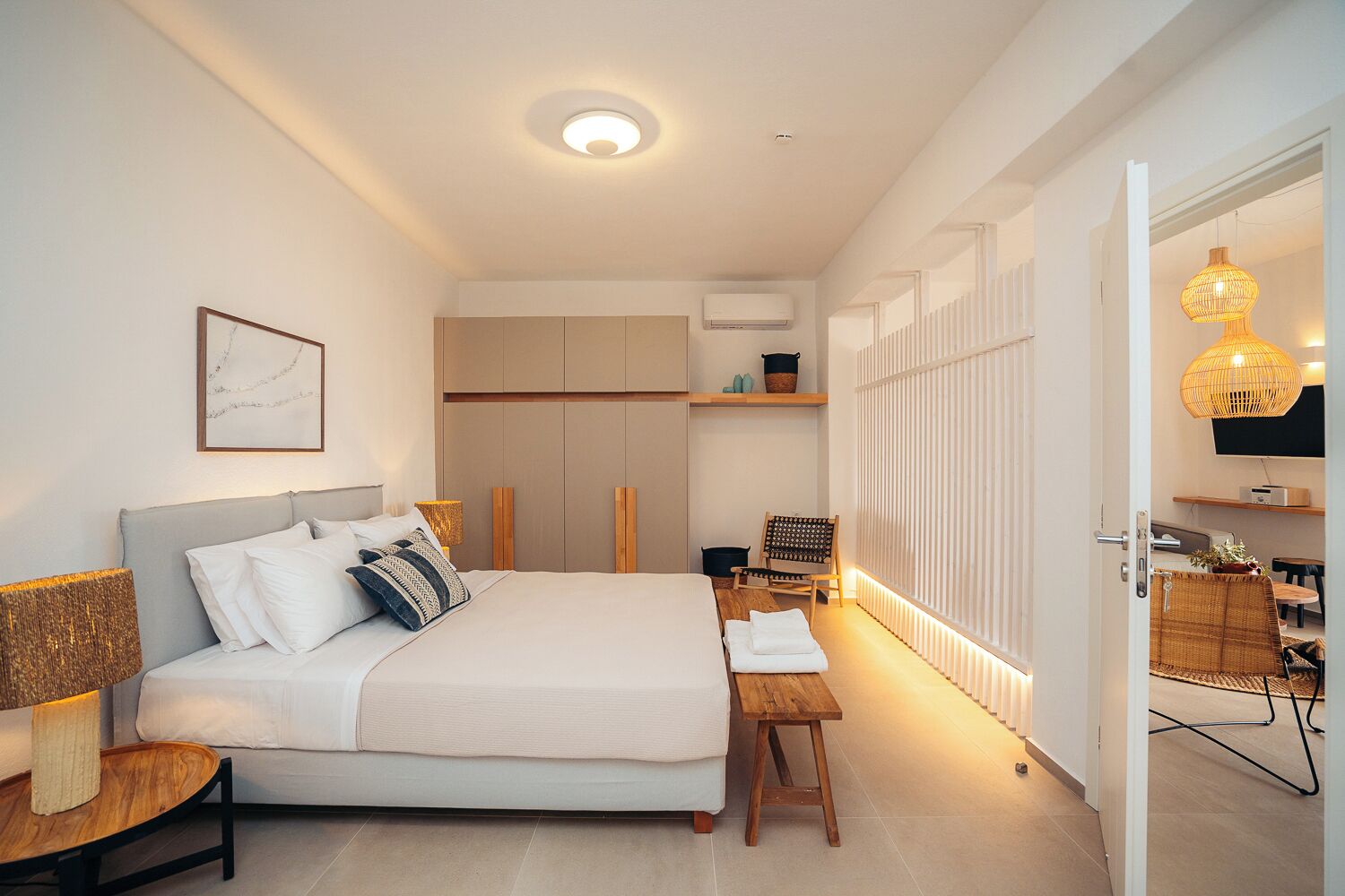 A modern bedroom with a bed, bedside table, and a chair. There is a wardrobe, a radiator, and a TV mounted on the wall.