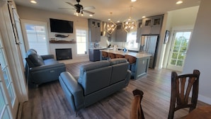 Una sala de estar moderna con chimenea, un televisor grande y una zona de comedor con una mesa y sillas de madera.