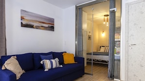 A modern living room with a blue sofa, a glass door leading to a bedroom, and a painting on the wall. - Navy Blue Apartment (Corfu)