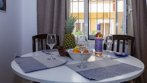 A round dining table with a white tablecloth, two chairs, a bowl of fruit, a bottle of wine, and two glasses. - Navy Blue Apartment (Corfu)