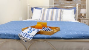 A neatly made bed with a blue quilt, a tray with orange juice, and a striped towel. - Navy Blue Apartment (Corfu)