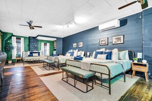 A modern bedroom with a large bed, two smaller beds, a bench, and a ceiling fan.