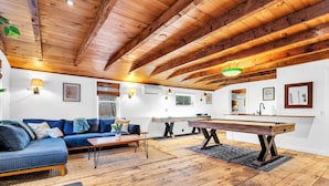 Un salon spacieux avec un plafond en bois, un canapé bleu, une table de billard et une table de jeu de fléchettes.