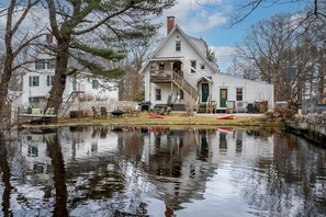A white colonial-style house with a large porch and a small pond in front.