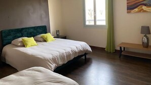 Hotellihuone, jossa on sänky, yöpöytä, lamppu, ikkuna verhoilla ja seinällä taulu.