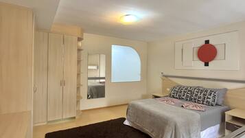 Relax in a serene bedroom with a large bed, wooden wardrobe, and a bedside table.