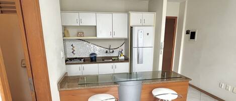 A modern kitchen with white cabinets, a stainless steel refrigerator, and two bar stools.