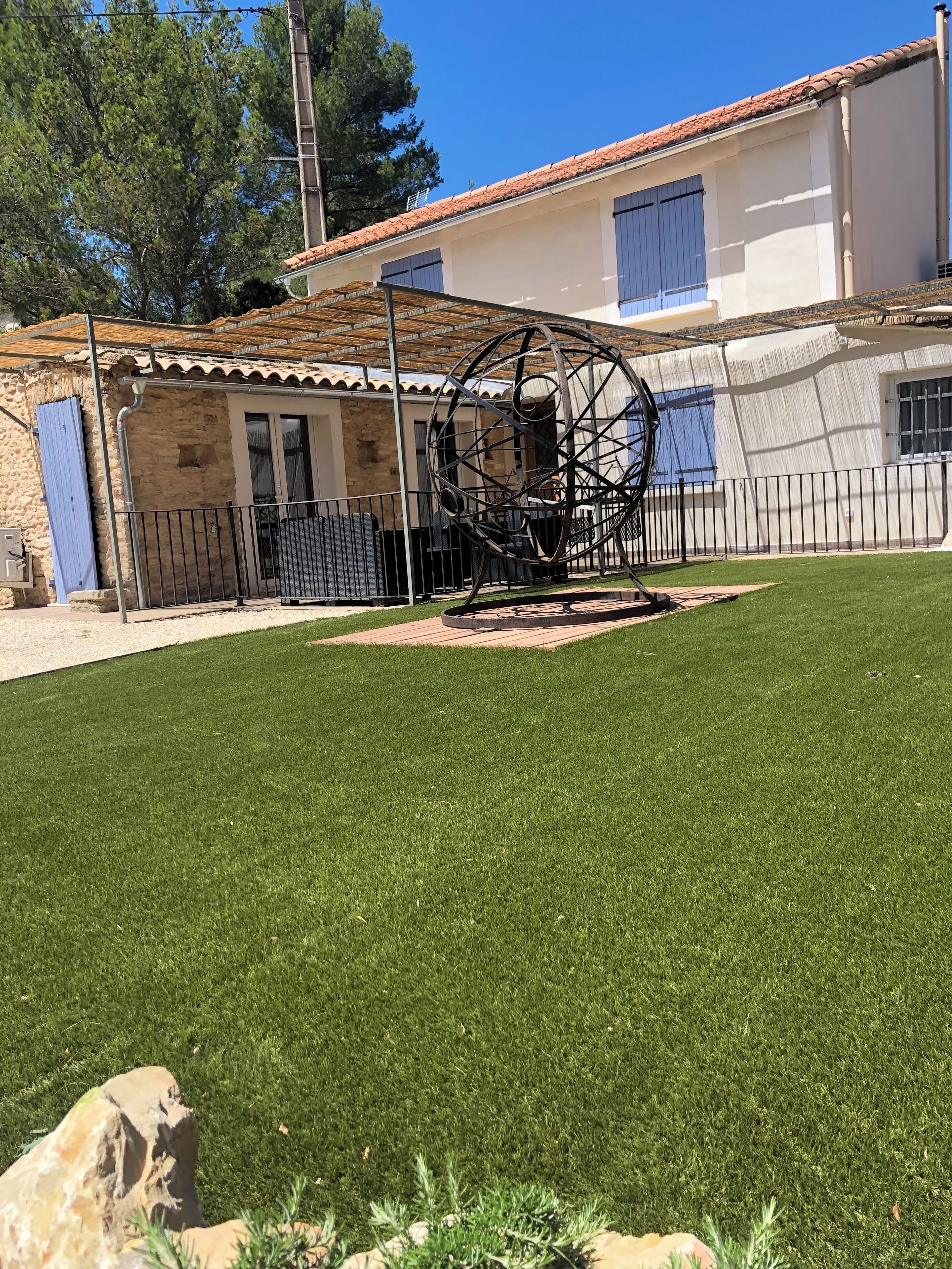 Un patio con una escultura de metal, un muro de piedra y un edificio con techo de tejas.