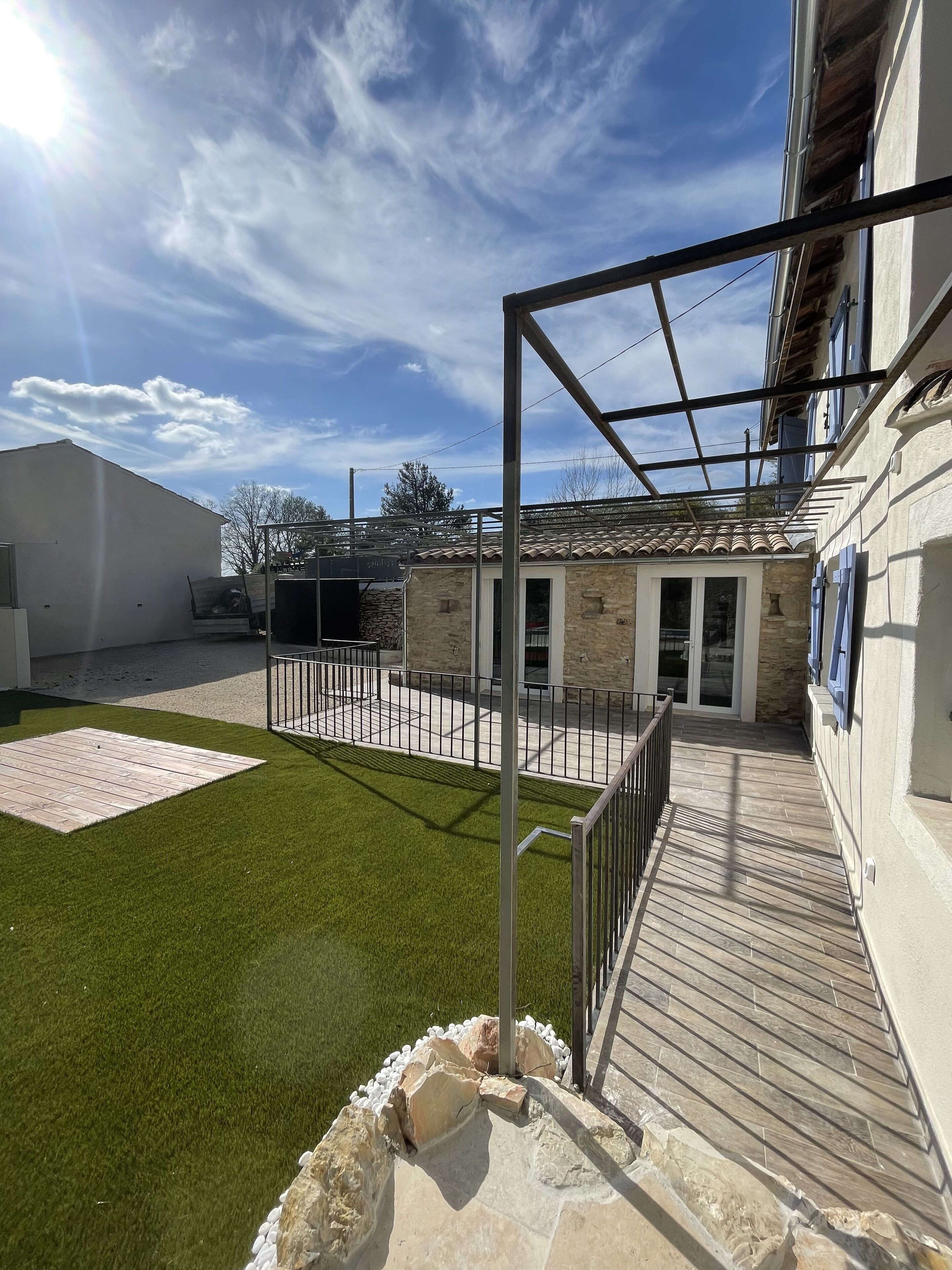 A courtyard with artificial grass, a stone pathway, and a metal pergola structure.