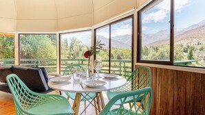Comedor con una mesa lista para dos personas, rodeado de amplios ventanales con vista a la montaña.