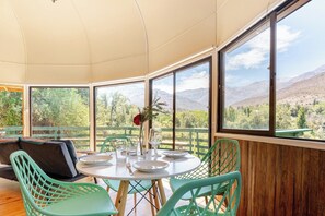 A dining area with a table set for two, surrounded by large windows offering a mountain view.