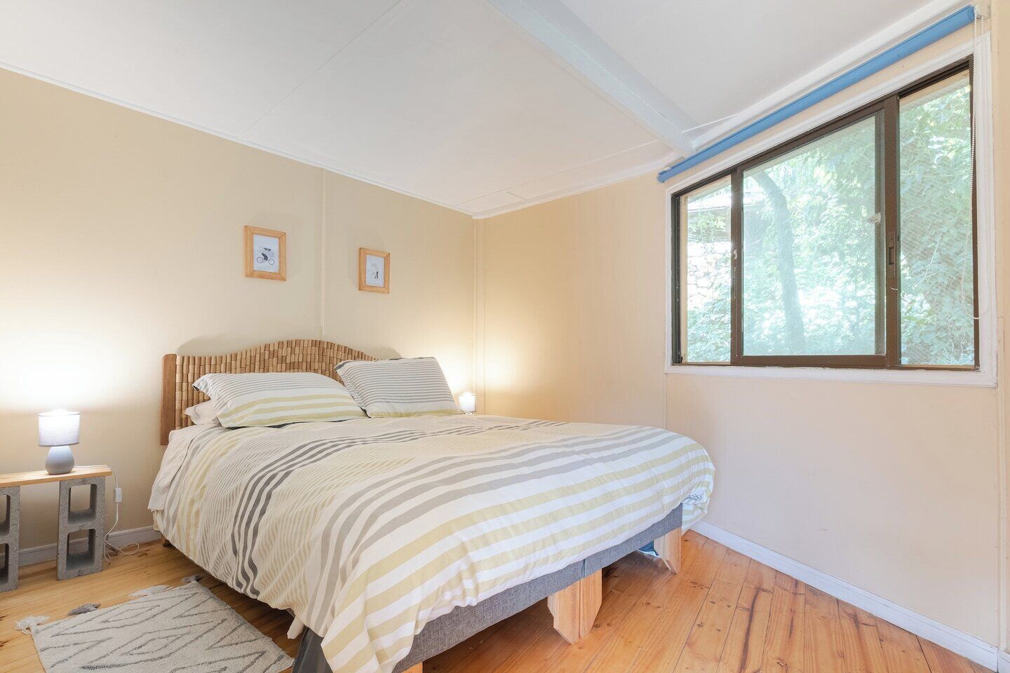 Ein Schlafzimmer mit einem Bett, Nachttischlampen, einem Fenster und einem gerahmten Bild an der Wand.