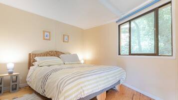 Ein Schlafzimmer mit einem Bett, Nachttischlampen, einem Fenster und einem gerahmten Bild an der Wand.