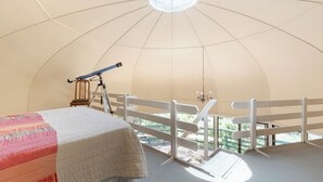 Una habitación abovedada con un telescopio, una cama y un balcón con barandilla blanca.