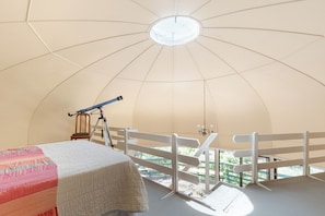 Una habitación abovedada con un telescopio, una cama y un balcón con barandilla blanca.
