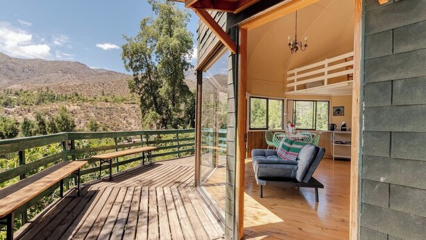 Una terraza de madera con bancos, un sofá y un comedor con vista a las montañas.