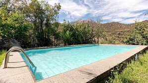 Una piscina con borde de piedra, rodeada de árboles y colinas.