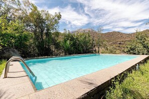 Una piscina con borde de piedra, rodeada de árboles y colinas.