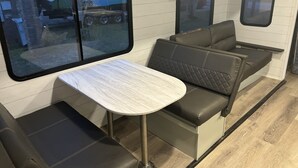 Un intérieur de camping-car compact comprenant une table à manger, un coin salon et une grande fenêtre.
