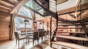 Een modern interieur met een houten trap, een eethoek met tafel en stoelen, en grote ramen met uitzicht op het exterieur.