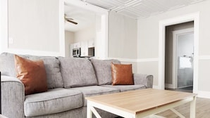 Ein Wohnzimmer mit einem grauen Ecksofa, zwei braunen Kissen und einem Holztisch.
