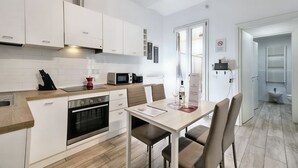 Une cuisine moderne avec des meubles blancs, un four encastré et un coin repas comprenant une table et des chaises.