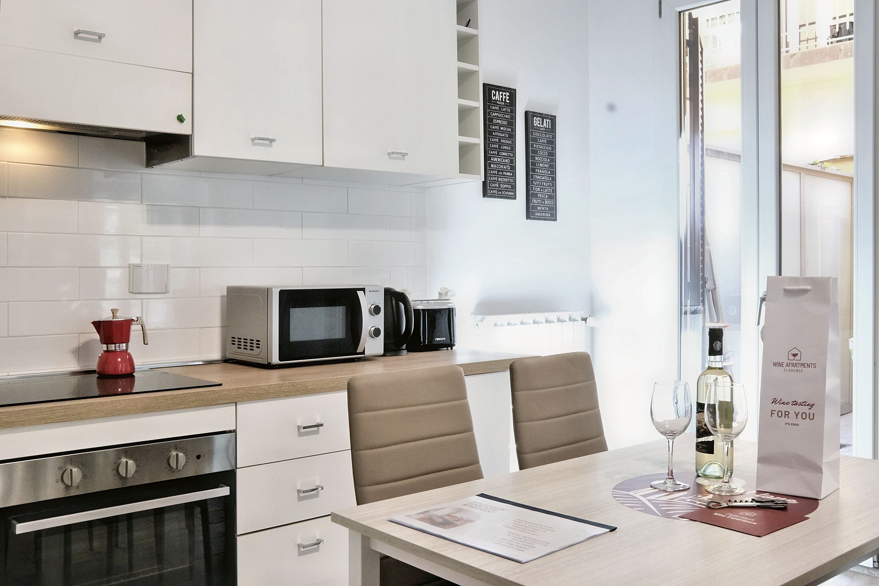 A modern kitchen with white cabinets, a microwave, a coffee maker, and a dining area with chairs and a table.