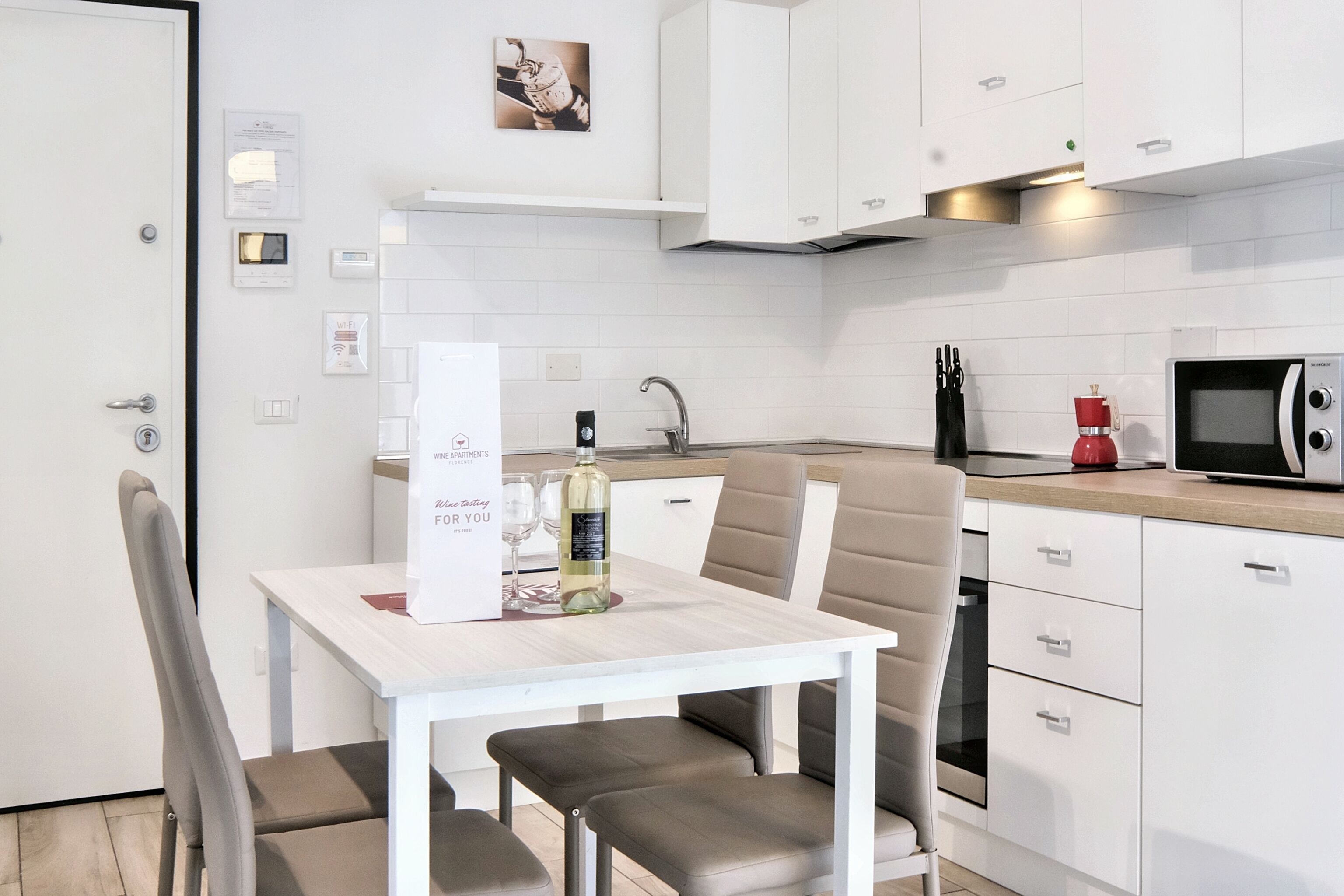 Een moderne keuken met witte kasten, een inbouwoven, een magnetron en een rode koffiemachine.