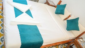 Una cama bien hecha con colcha blanca y azul verdoso, almohadas azul verdosas y una toalla blanca doblada.