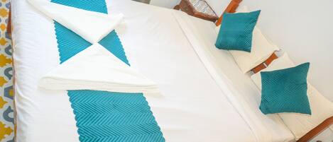 A neatly made bed with a white and teal bedspread, teal pillows, and a folded white towel.