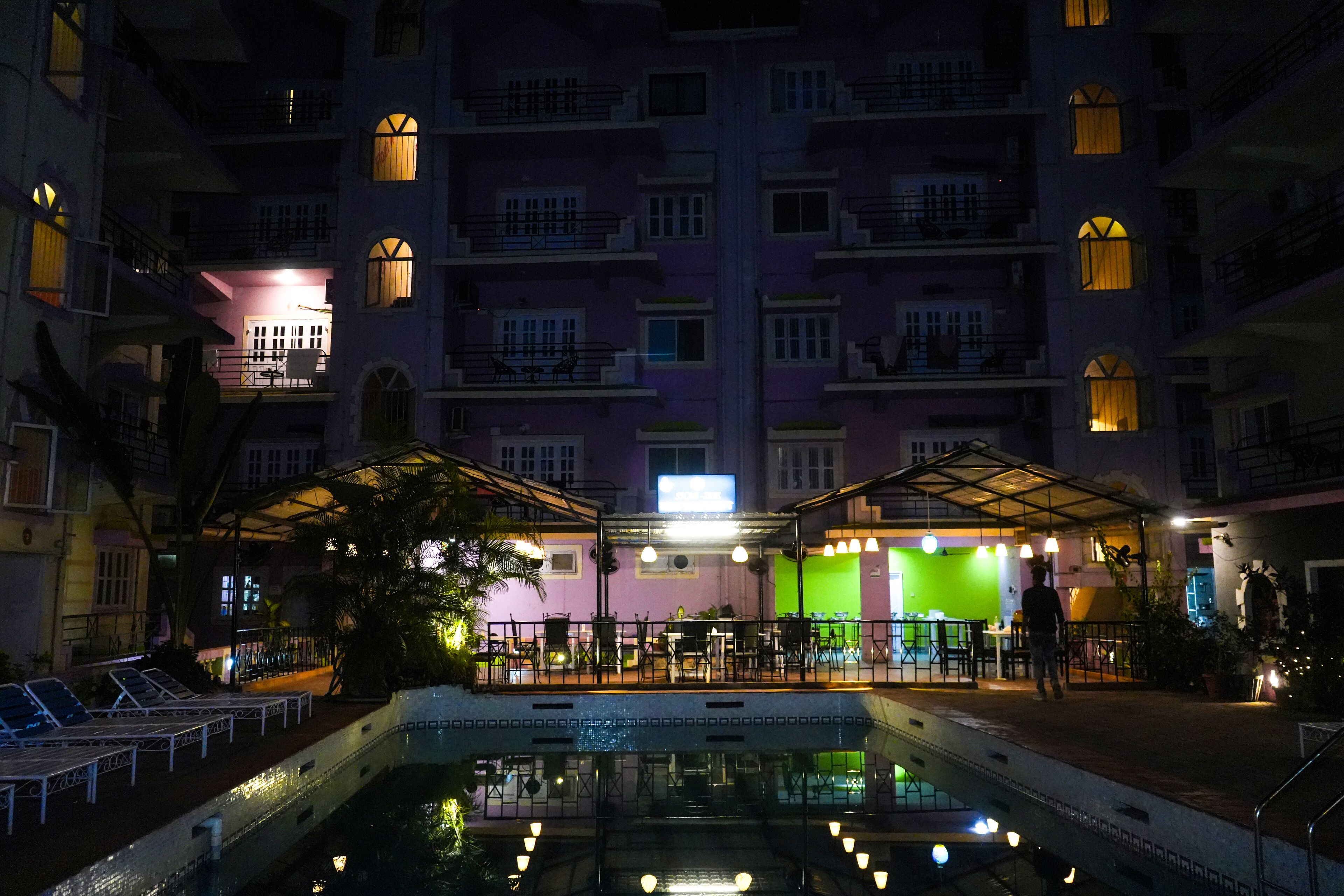 A nighttime view of a hotel with a pool, outdoor seating area, and multiple balconies.
